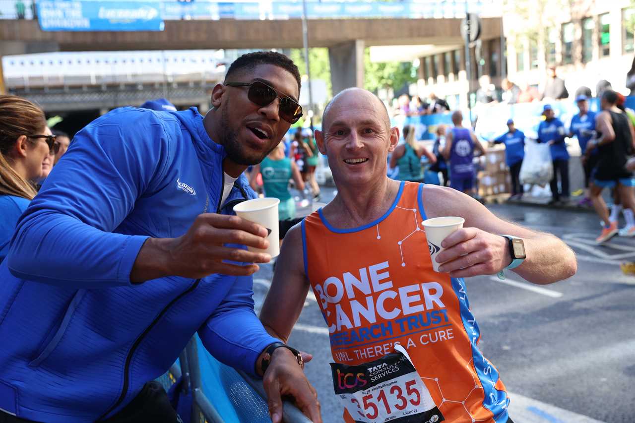As Tyson Fury talks, Anthony Joshua gives drinks to London Marathon runners who stopped for selfies.