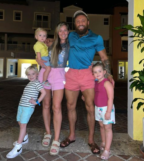 Conor McGregor beams while cuddling Dee Devlin, his fiancee, and their children as the UFC star recovers after an injury.