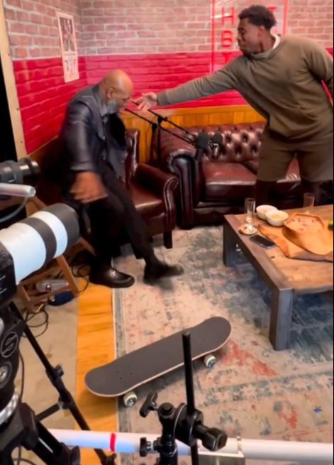 Mike Tyson, boxing legend, attempts to do a skateboard trick before falling backwards into an office chair